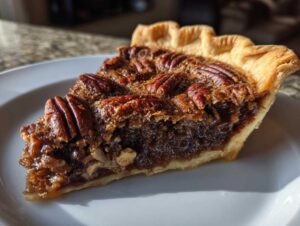 A close-up shot of a slice of decadent chocolate pecan pie on a white plate.