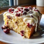 A close-up of a slice of Cranberry Bliss Bars, topped with white icing and dried cranberries.