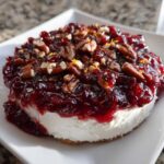 A close-up of a festive cranberry cream cheese dip topped with pecans and orange zest.
