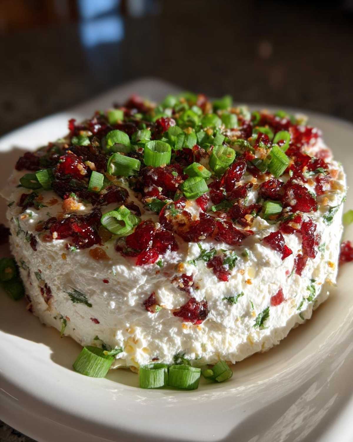 A festive Cranberry Jalapeno Cream Cheese Dip topped with chopped green onions and dried cranberries.