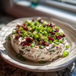 A close-up of a cranberry jalapeno cream cheese dip, garnished with chopped green onions and dried cranberries.