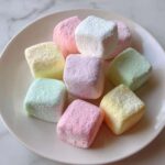 A close-up of pastel-colored cream cheese mints dusted with powdered sugar on a white plate.