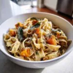 A close-up of creamy butternut squash pasta topped with roasted squash cubes and fresh sage leaves.