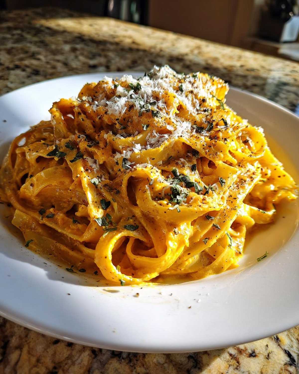 A close-up of creamy pumpkin pasta, topped with grated Parmesan cheese and fresh herbs.