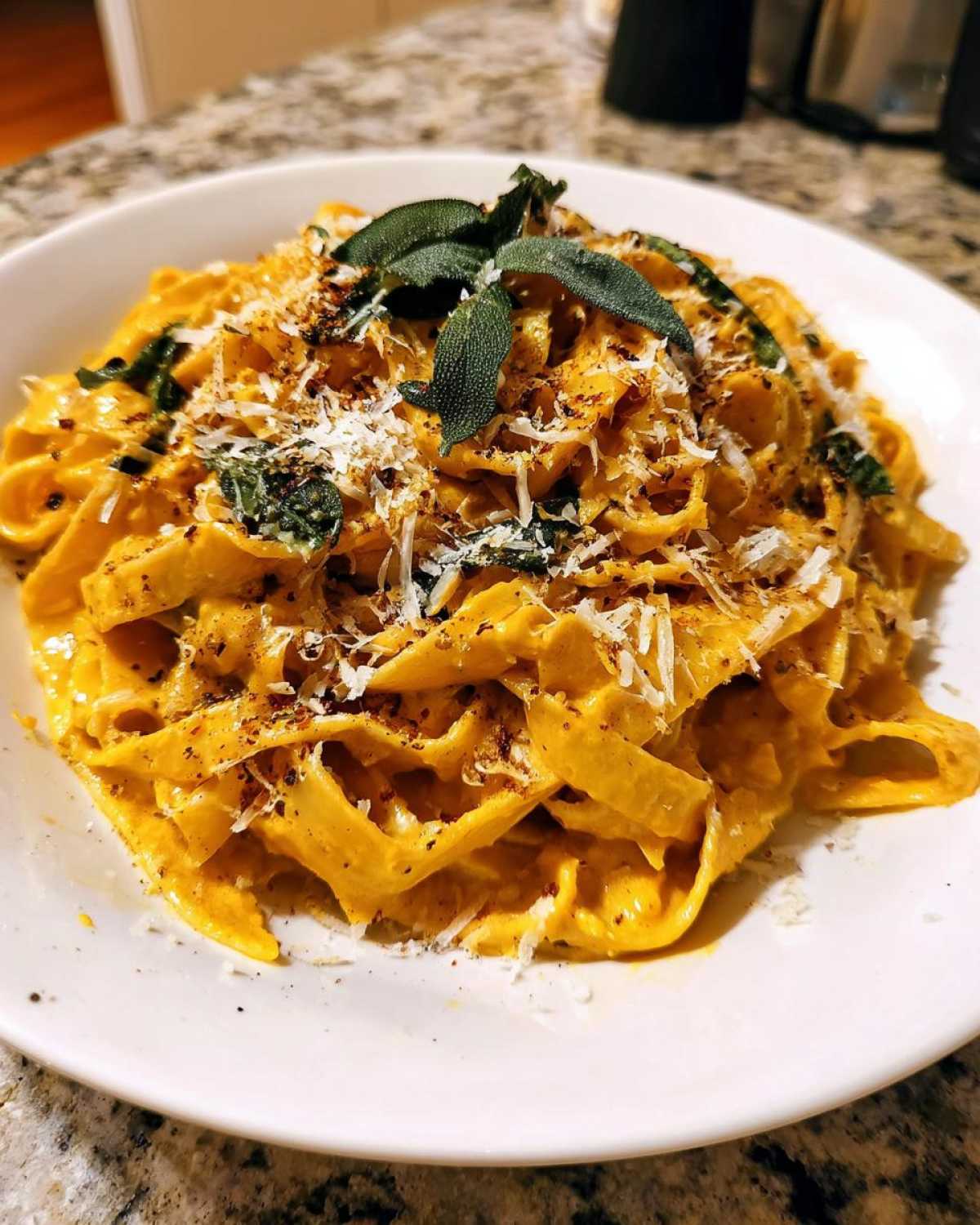 A close-up of creamy pumpkin pasta topped with fresh sage leaves and grated Parmesan cheese.
