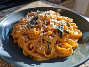 A close-up of creamy pumpkin pasta topped with fresh sage leaves and grated Parmesan cheese.