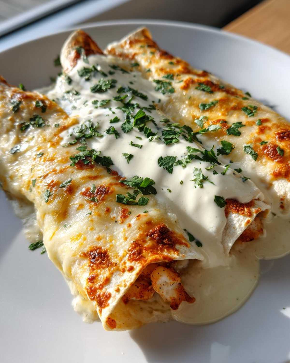 Three creamy shrimp enchiladas topped with melted cheese and fresh parsley, served on a white plate.