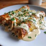 Three creamy shrimp enchiladas covered in sauce and chopped parsley on a white plate.