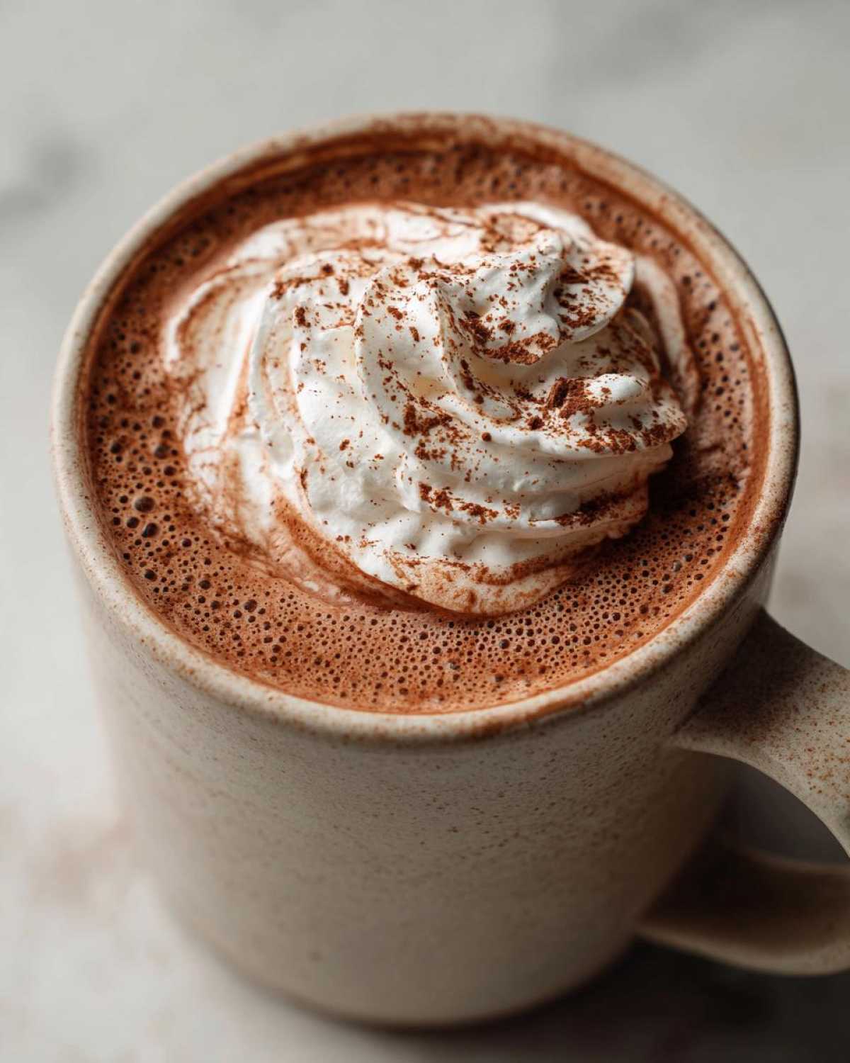 A close-up of a mug filled with rich crockpot hot chocolate, topped with fluffy whipped cream and a sprinkle of cocoa powder.