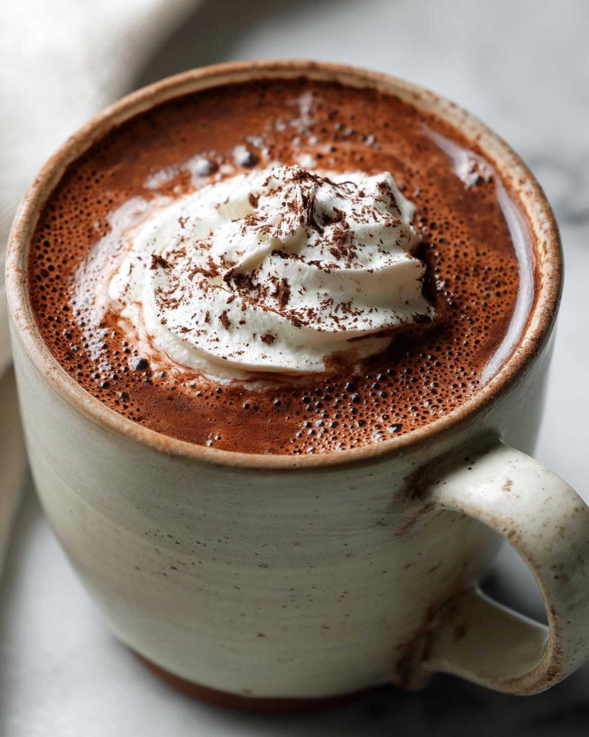 A close-up of a steaming mug of crockpot hot chocolate topped with whipped cream and chocolate shavings.