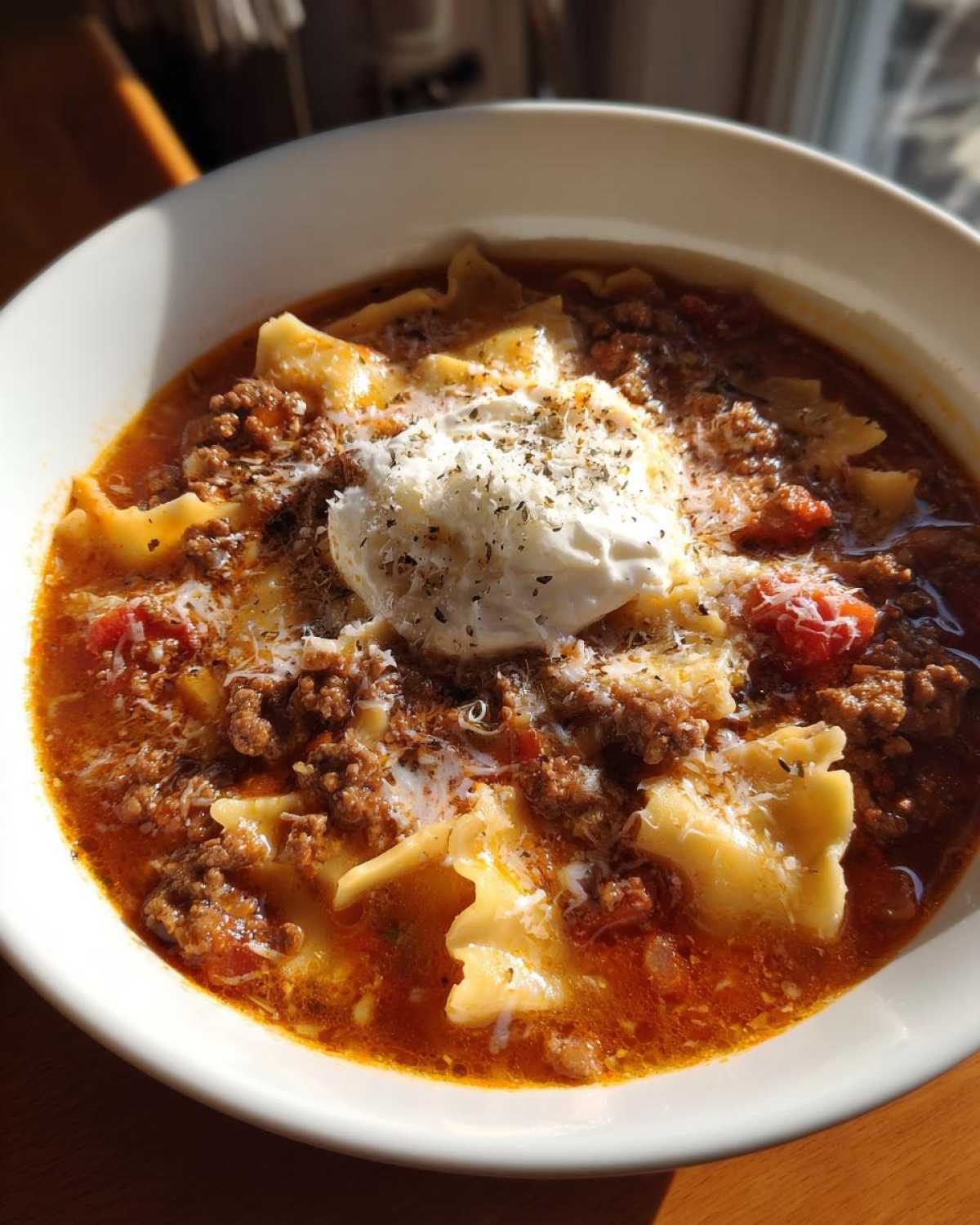 A bowl of hearty crockpot lasagna soup topped with ricotta cheese, parmesan, and herbs.
