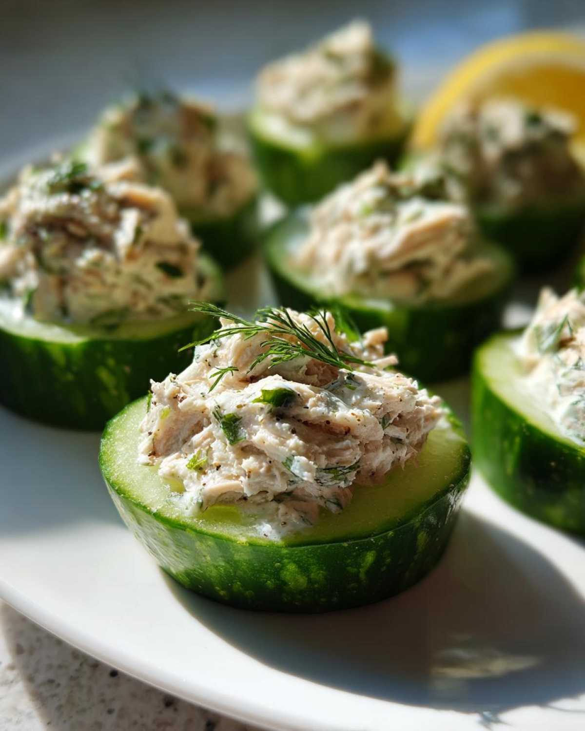 Cucumber tuna salad appetizers on a white plate, garnished with dill and a lemon wedge.