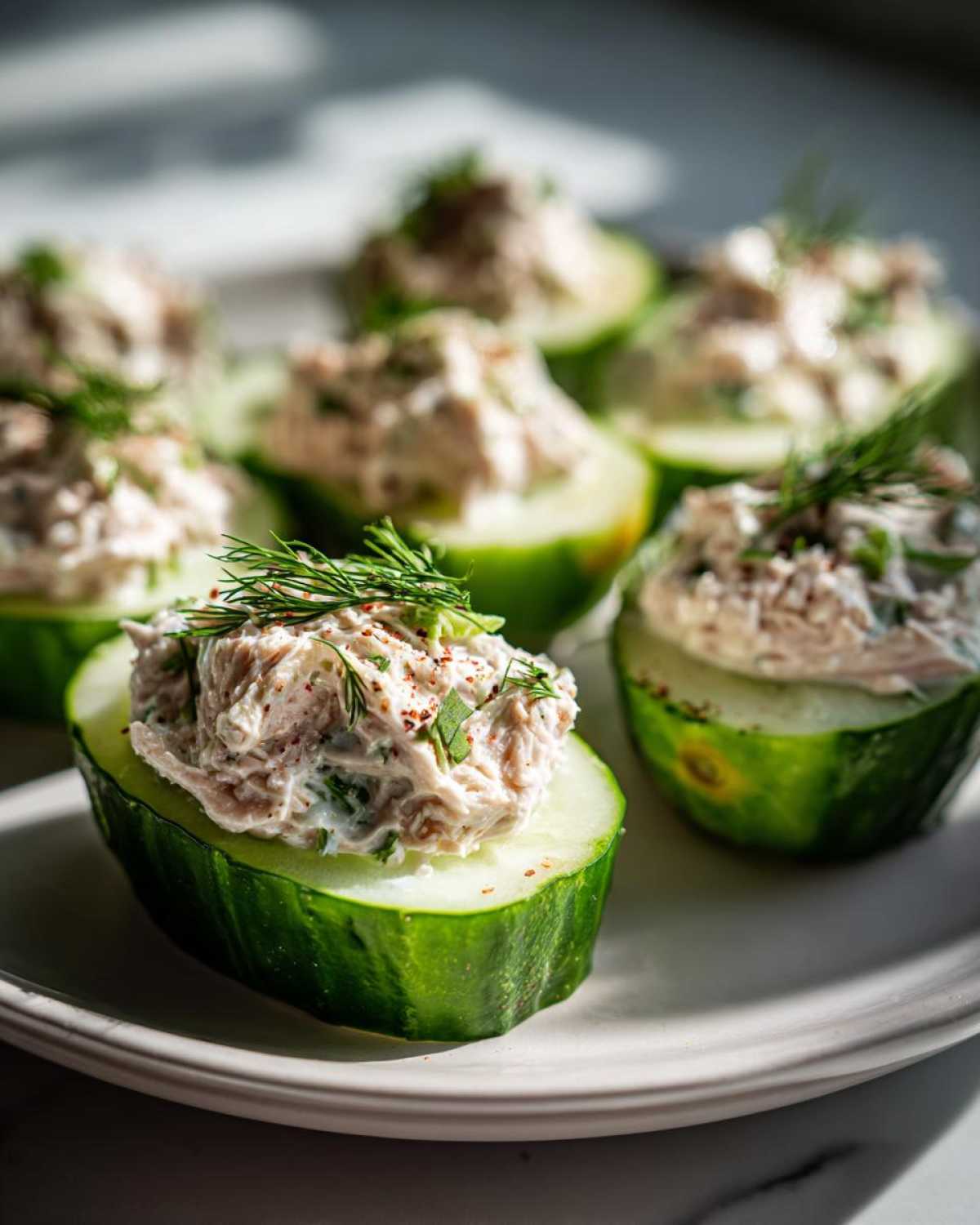 Close-up of cucumber tuna salad bites, featuring fresh cucumber slices topped with creamy tuna salad and dill.