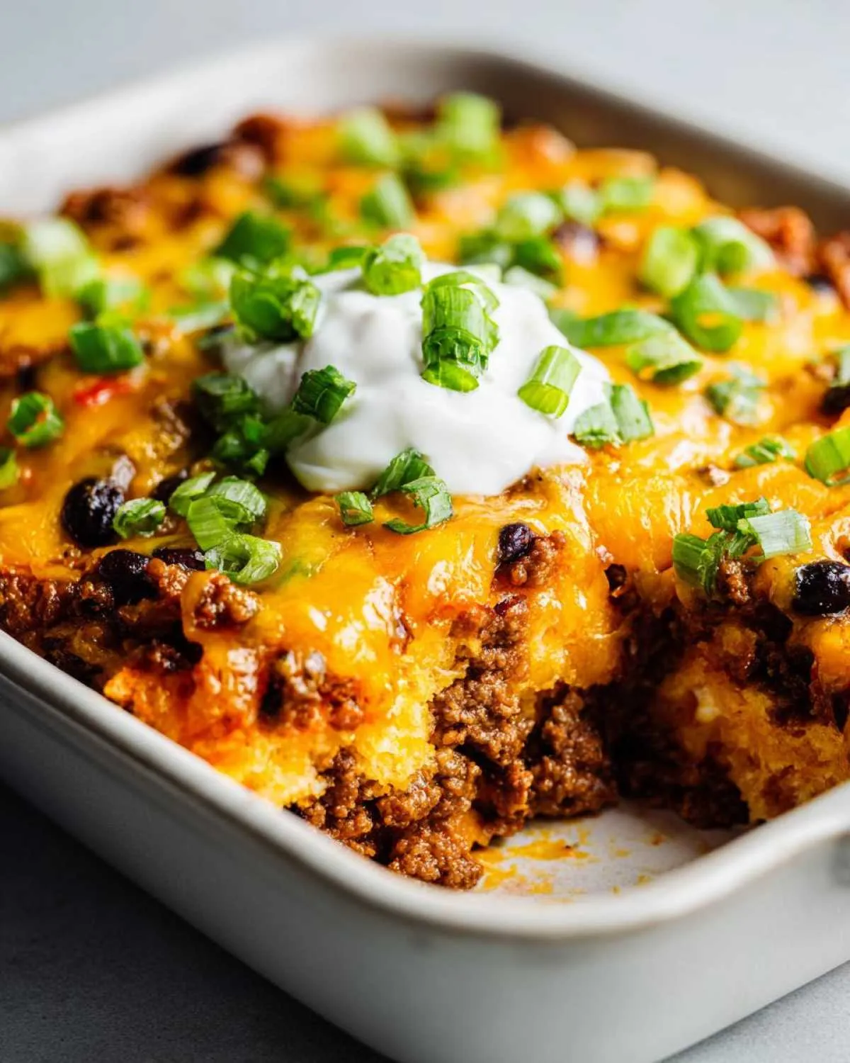 Close-up of a cheesy Dorito casserole topped with sour cream and green onions. Ready to eat Dorito casserole recipe.