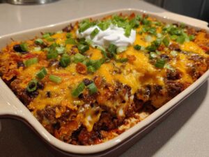 Baked Dorito casserole recipe with melted cheese, beef, black beans, green onions, and sour cream topping.