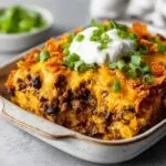 A slice of Dorito casserole recipe with beef, black beans, cheese, Doritos, sour cream, and green onions.