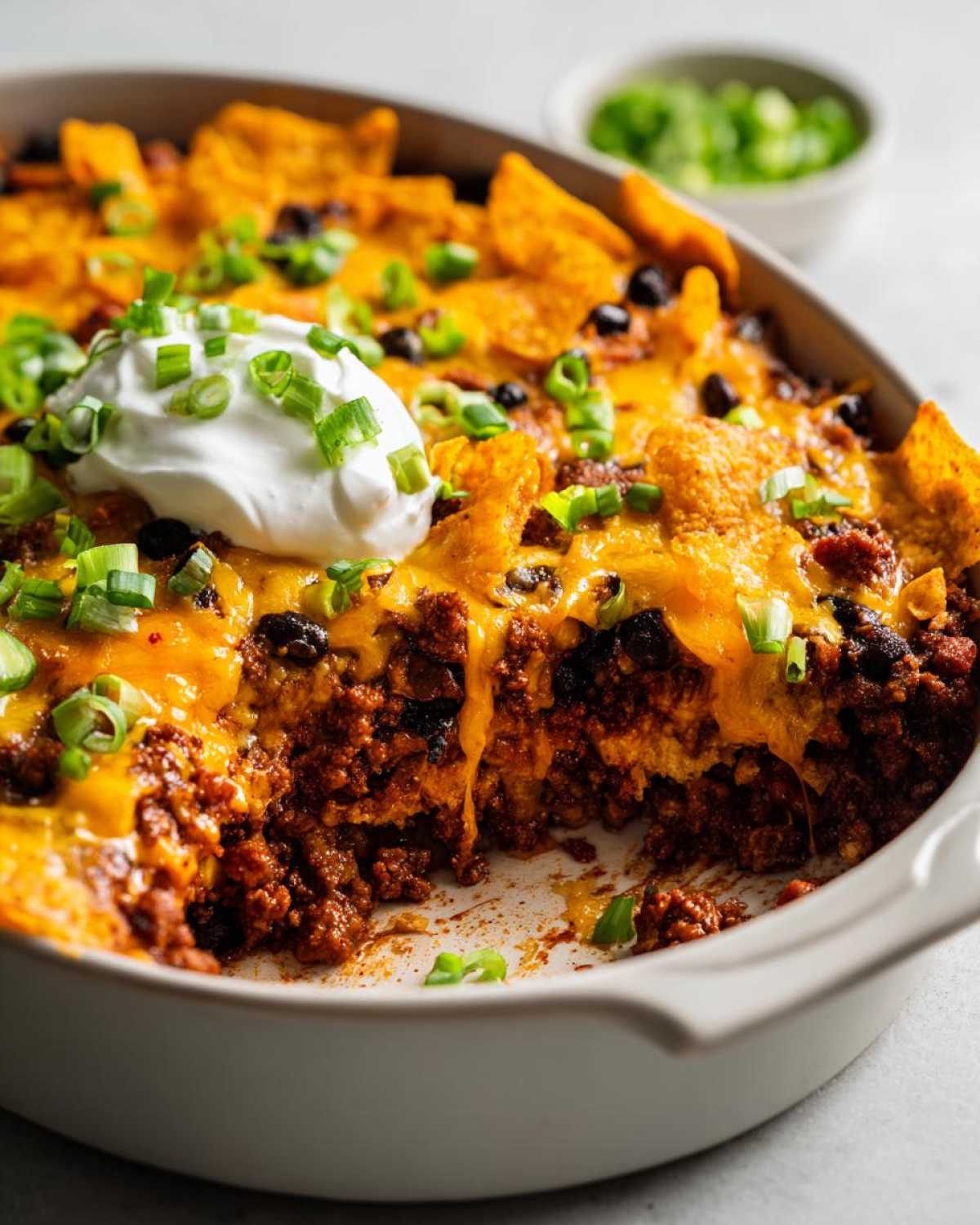 A cheesy Dorito casserole recipe, topped with sour cream and green onions, in a baking dish.