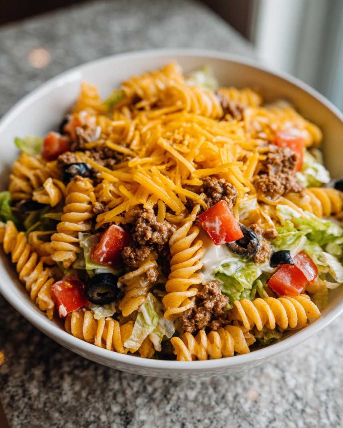 A vibrant bowl of Dorito taco salad pasta with lettuce, tomatoes, olives, beef, and shredded cheese.