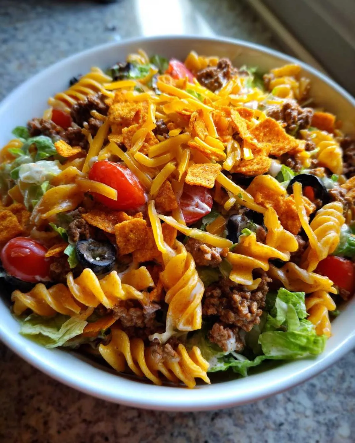 A bowl of Dorito taco salad pasta with lettuce, tomatoes, olives, ground beef, and crushed Doritos.