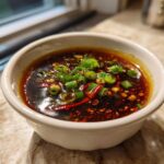 A bowl of flavorful dumpling sauce without soy sauce, garnished with green onions and chili flakes.