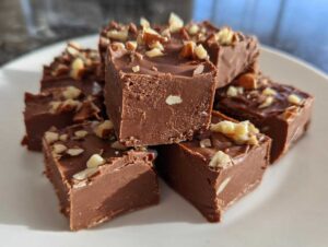 A stack of homemade fudge recipe squares topped with chopped nuts on a white plate.