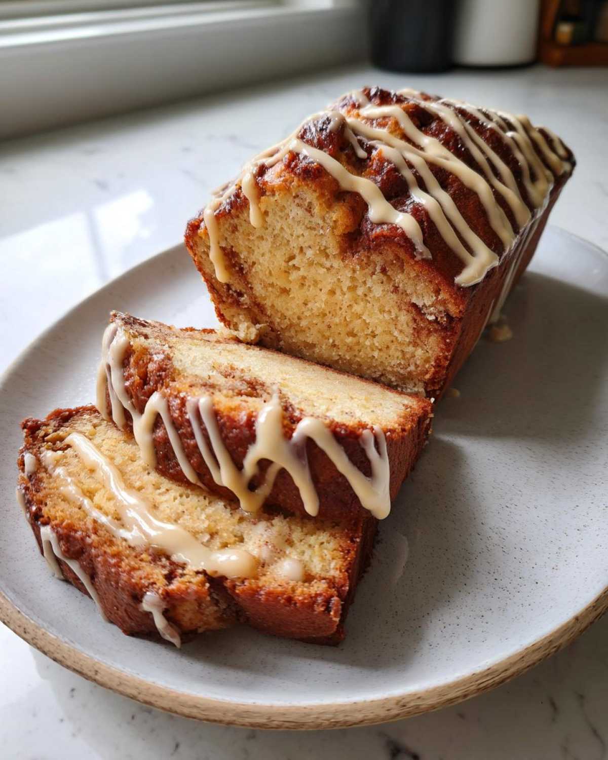 Close-up of a loaf of eggnog bread, sliced, with a drizzled spiced glaze.