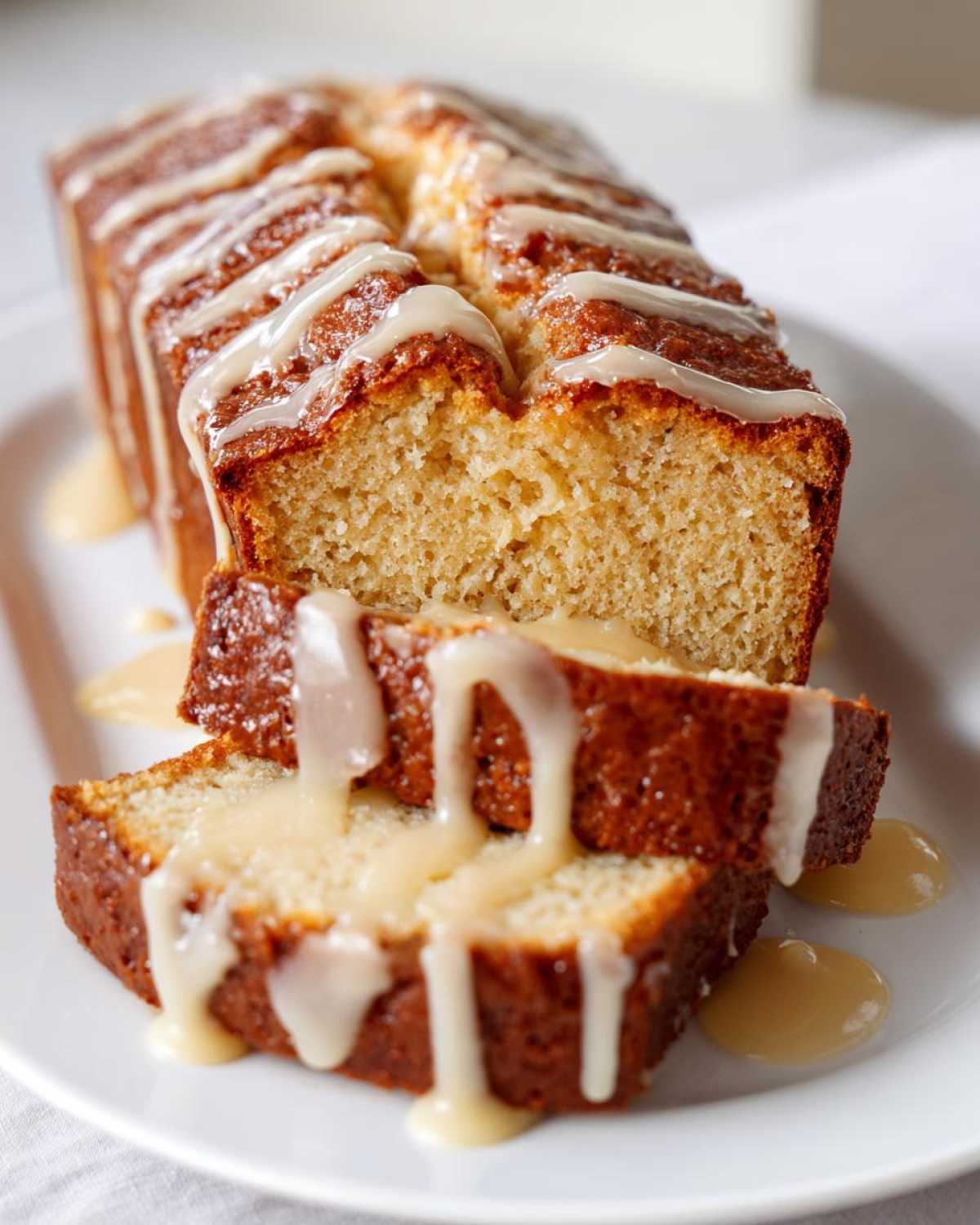 Close-up of two slices of eggnog bread on a white plate, drizzled with a creamy spiced glaze.