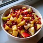 A colorful bowl of fall fruit salad with apples and pomegranate seeds.