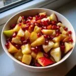 A colorful bowl of fall fruit salad with apples and pomegranate seeds.