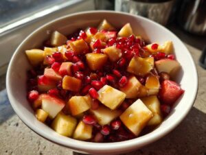 A bowl of fresh fall fruit salad featuring apples and pomegranate seeds, glistening with a light glaze.