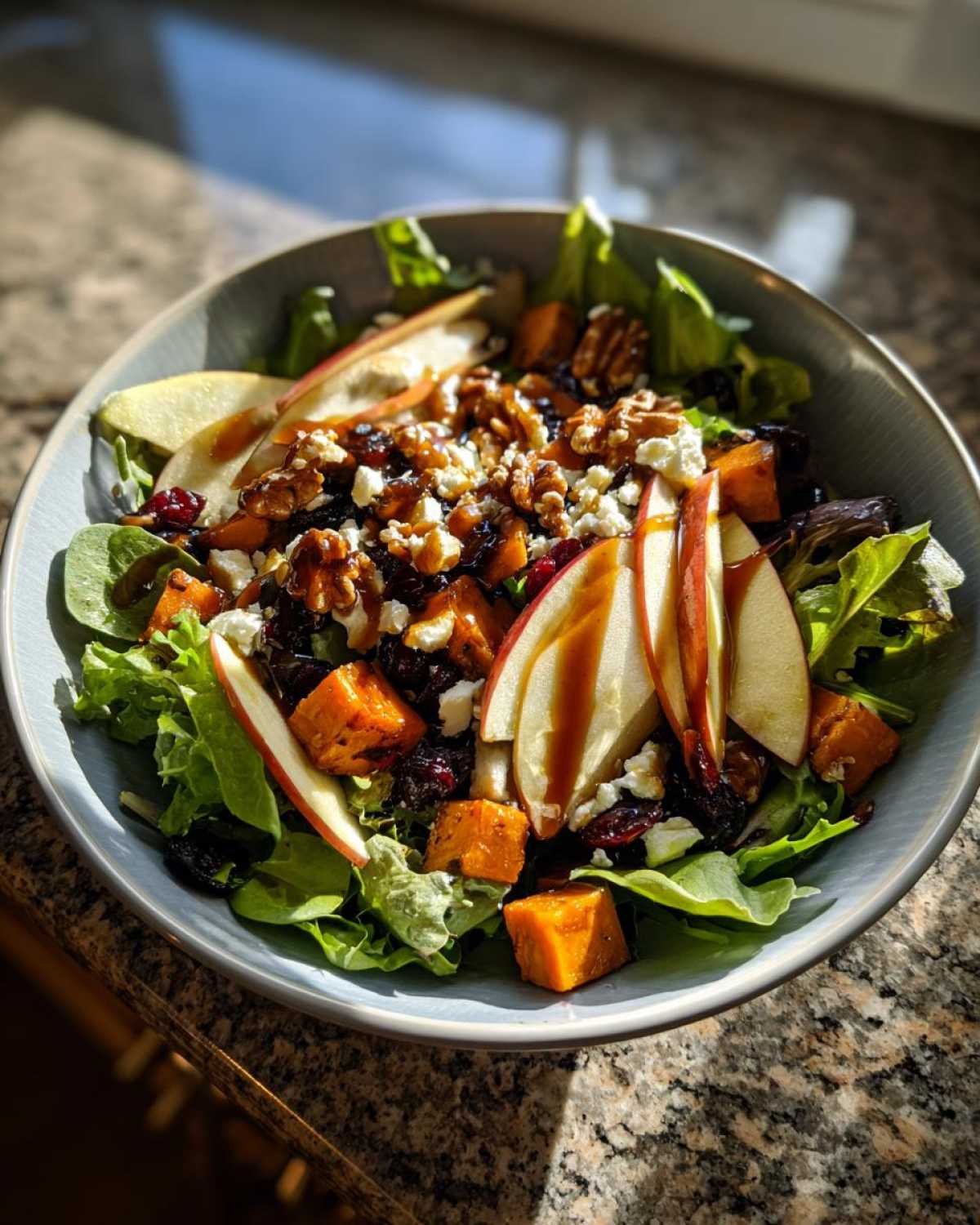 A close-up of a hearty fall harvest salad with roasted butternut squash, apples, walnuts, cranberries, and feta cheese, drizzled with maple vinaigrette.