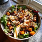 A delicious bowl of fall harvest salad featuring roasted butternut squash, apple slices, walnuts, cranberries, and feta cheese.