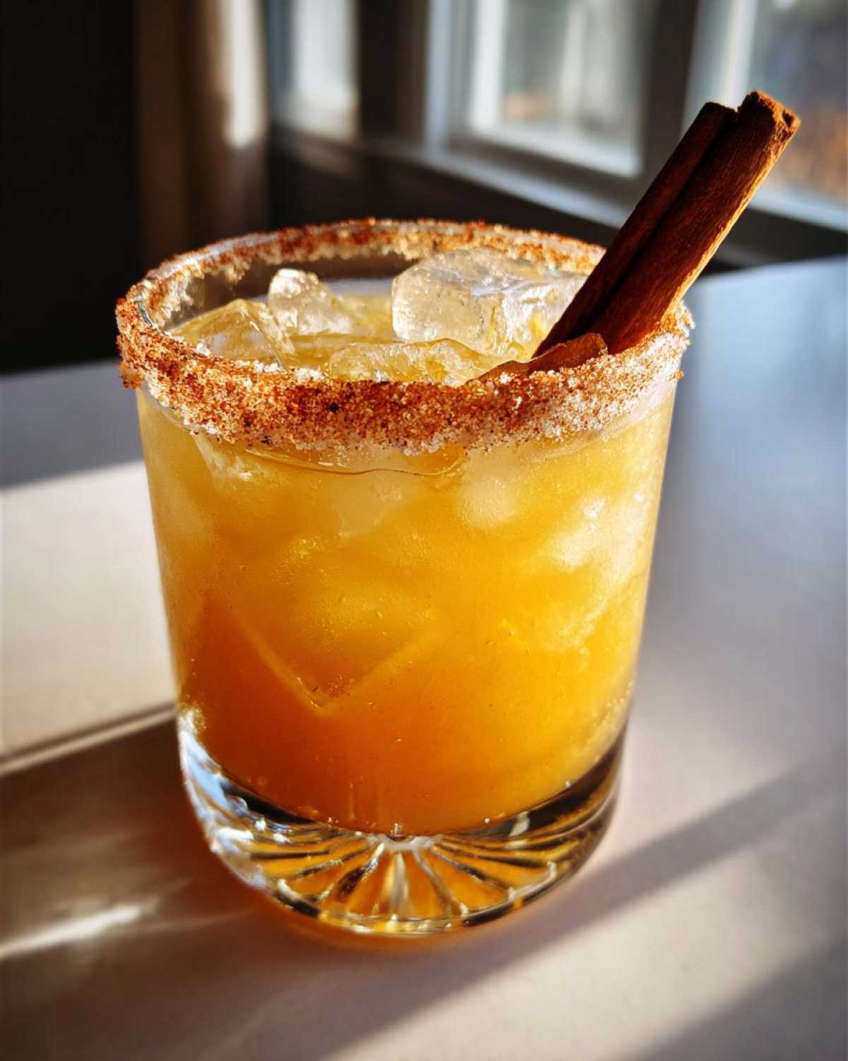 A vibrant fall margarita in a glass with a spiced rim and cinnamon stick garnish.