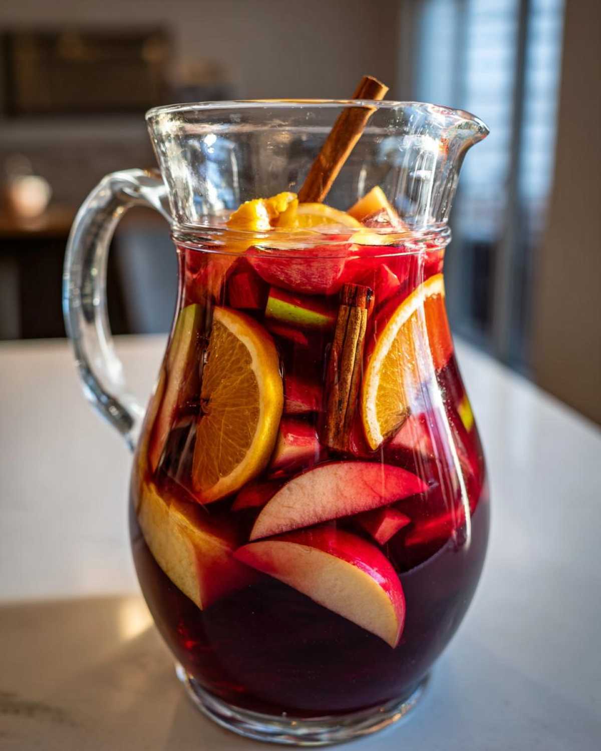 A glass pitcher filled with vibrant fall sangria, featuring apples, oranges, and cinnamon sticks.