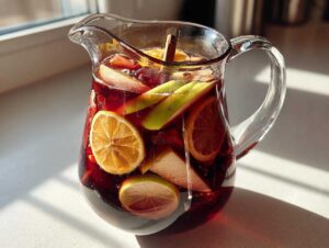 A glass pitcher filled with vibrant fall sangria, featuring apples, oranges, and a cinnamon stick.