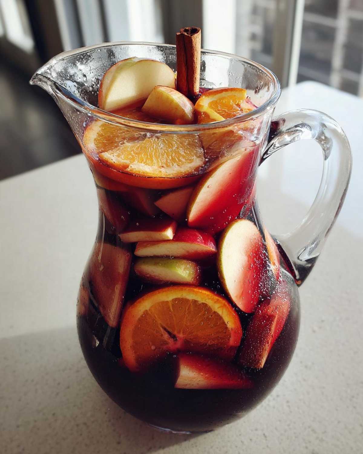 Pitcher of vibrant fall sangria filled with apples, oranges, and cinnamon sticks.