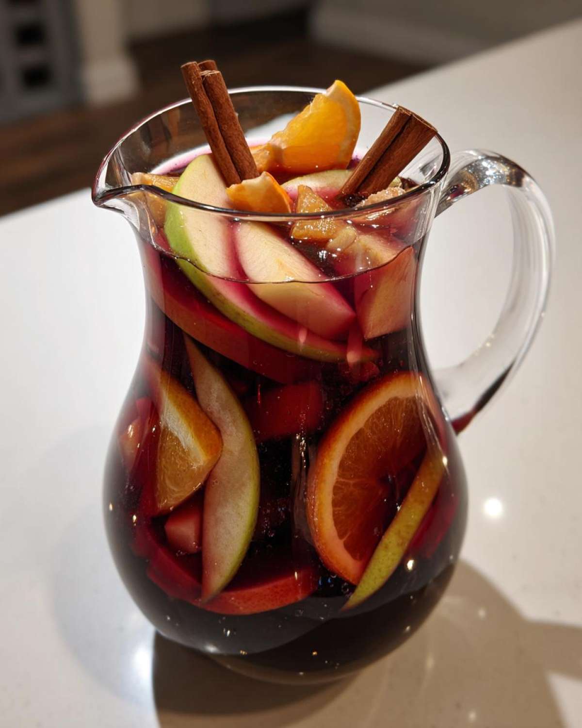 A glass pitcher filled with vibrant fall sangria, featuring apples, oranges, cinnamon sticks, and red wine.