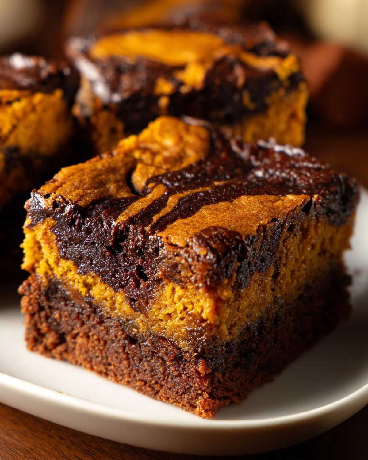 Close-up of a fudgy pumpkin brownie with chocolate swirls on a white plate.