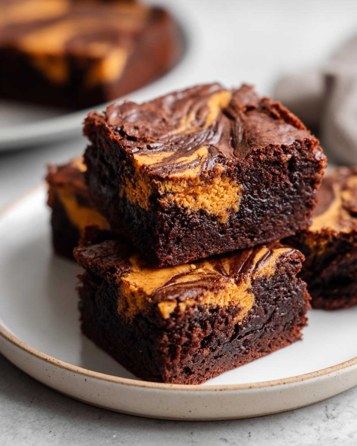 Close-up of stacked fudgy pumpkin brownies with peanut butter swirls on a white plate.