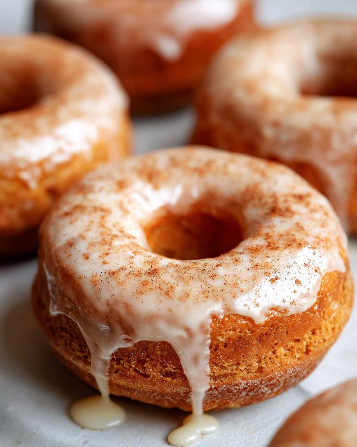 Close-up of a glazed pumpkin donut with a sprinkle of spice. Glaze drips down the side.