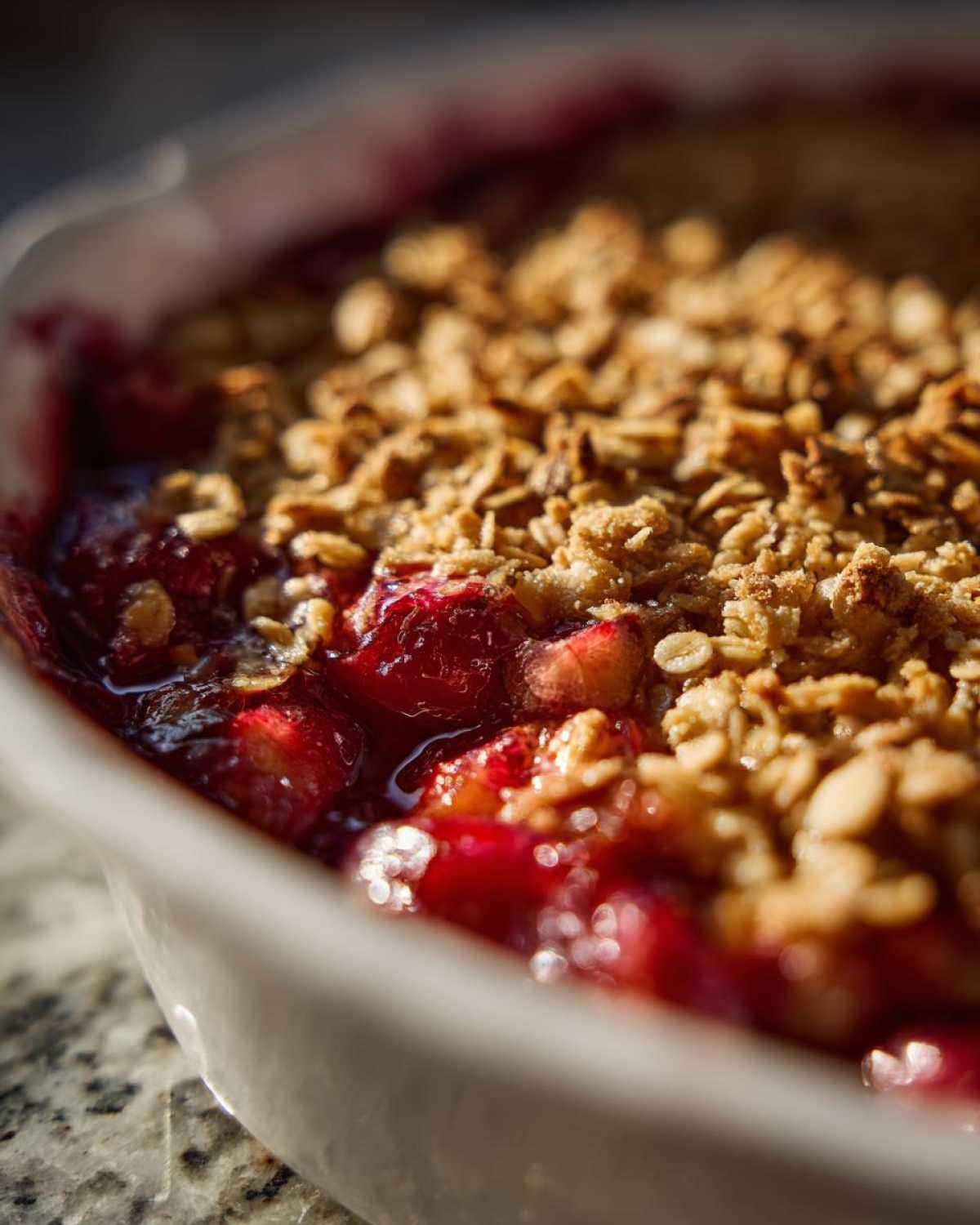 Close-up of a gluten free sour cherry crisp with a golden oat topping in a white baking dish.