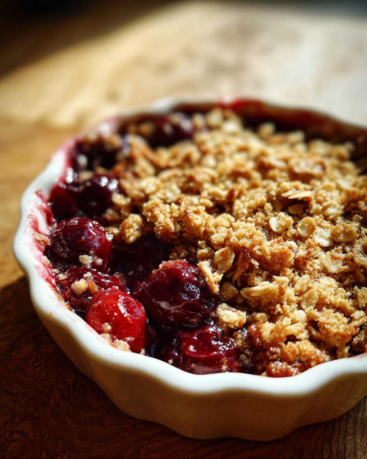Close-up of a gluten free sour cherry crisp in a white dish, showing the cherry filling and golden brown topping.