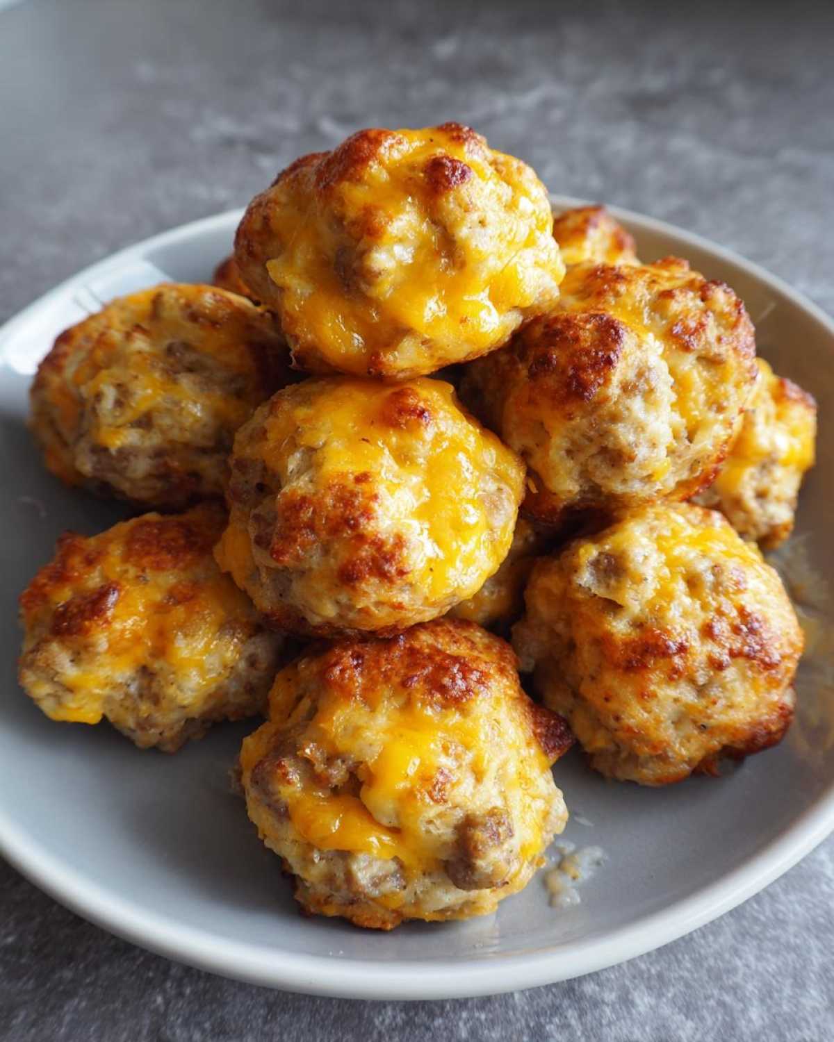 A pile of golden brown sausage balls topped with melted cheddar cheese on a grey plate.