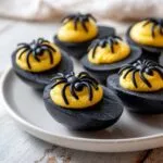 Close-up of black Halloween deviled eggs topped with yellow filling and a black spider decoration.