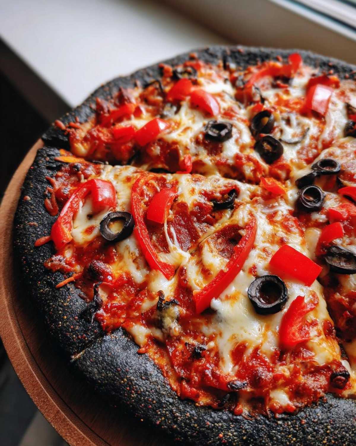 Close-up of a Halloween pizza with black crust, red peppers, olives, and melted cheese.