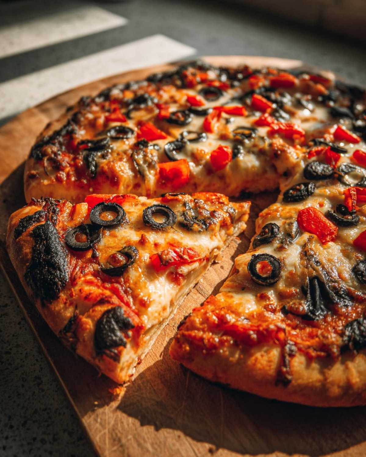 A freshly baked Halloween pizza with black olives and red peppers on a wooden board, ready to be served.