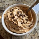 A bowl of high protein cookie dough dip topped with chocolate chips and a spoon.
