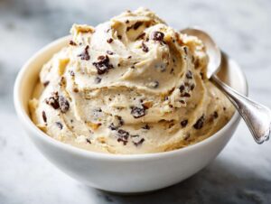 A bowl of creamy high protein cookie dough dip with chocolate chips, ready to eat with a spoon.