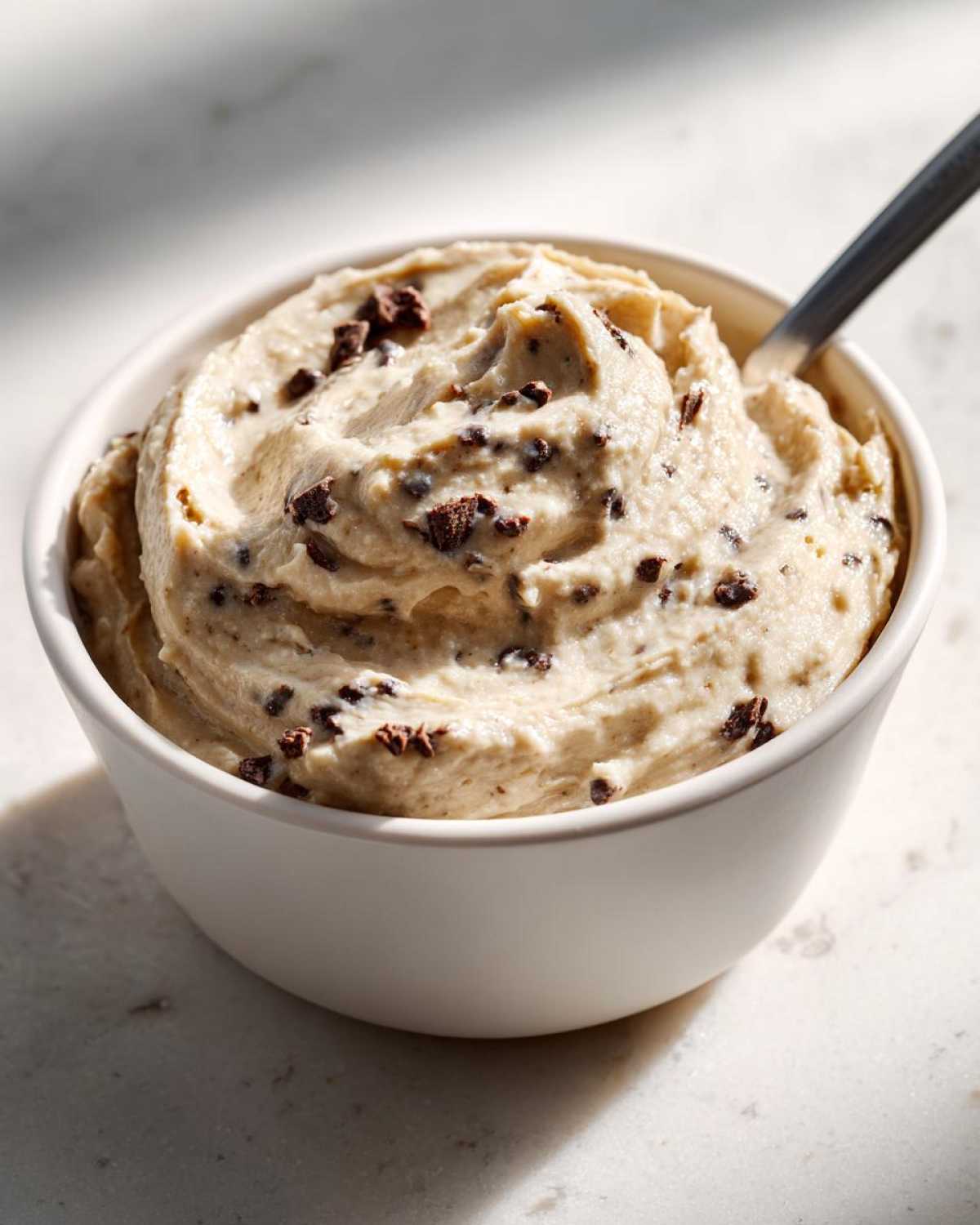 Bowl of creamy high protein cookie dough dip with chocolate chips and a spoon.
