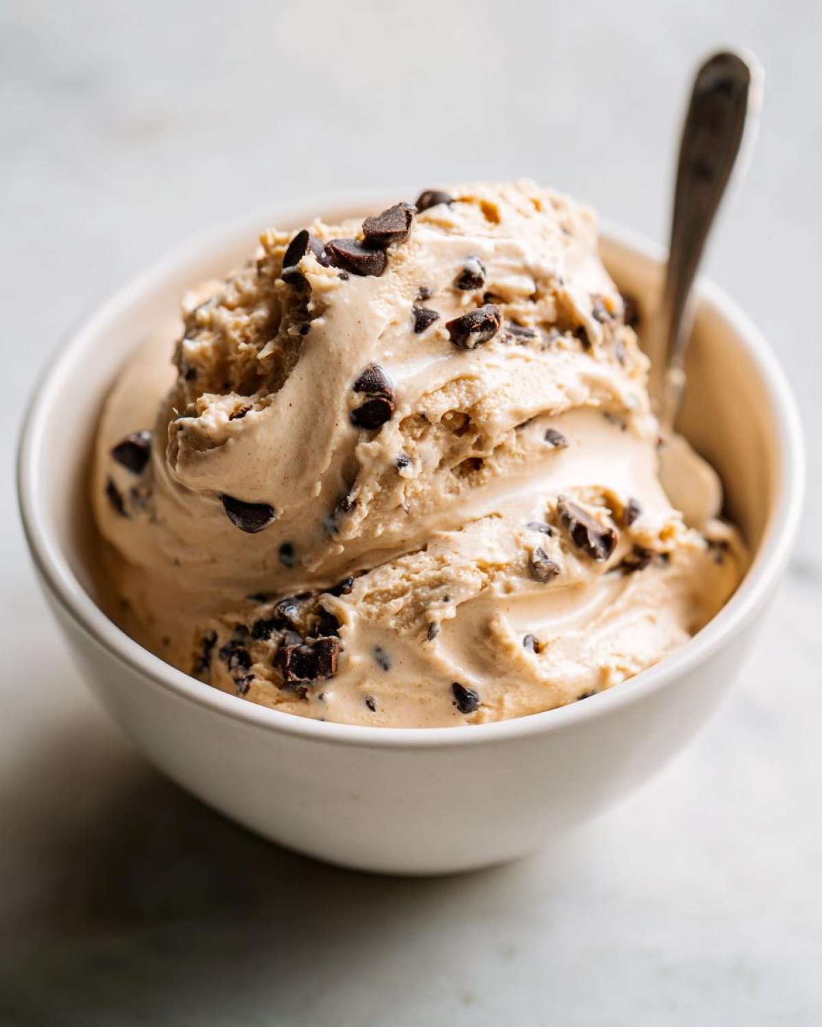 A bowl of creamy high protein cookie dough dip, topped with chocolate chips and a spoon.